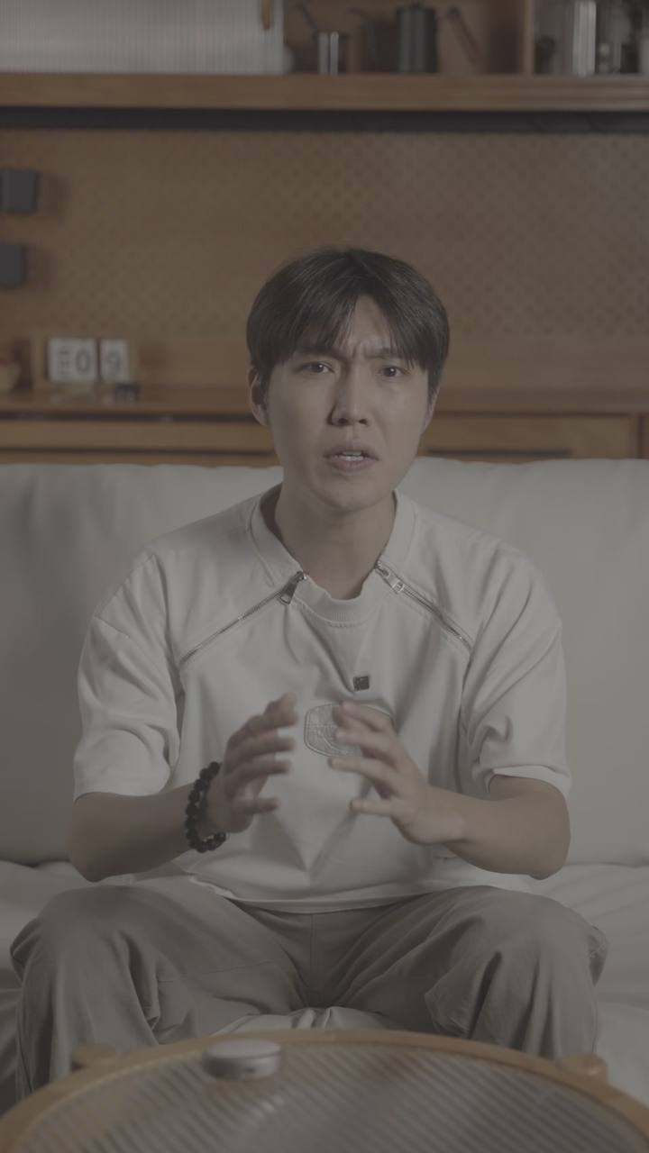 原始实拍 · 白T男性横评口播原镜:沙发与后方木格柜。