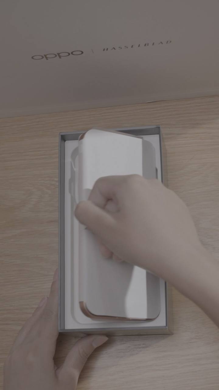 原始实拍 · 浅木桌上从包装取出手机，保护纸仍在机身上。